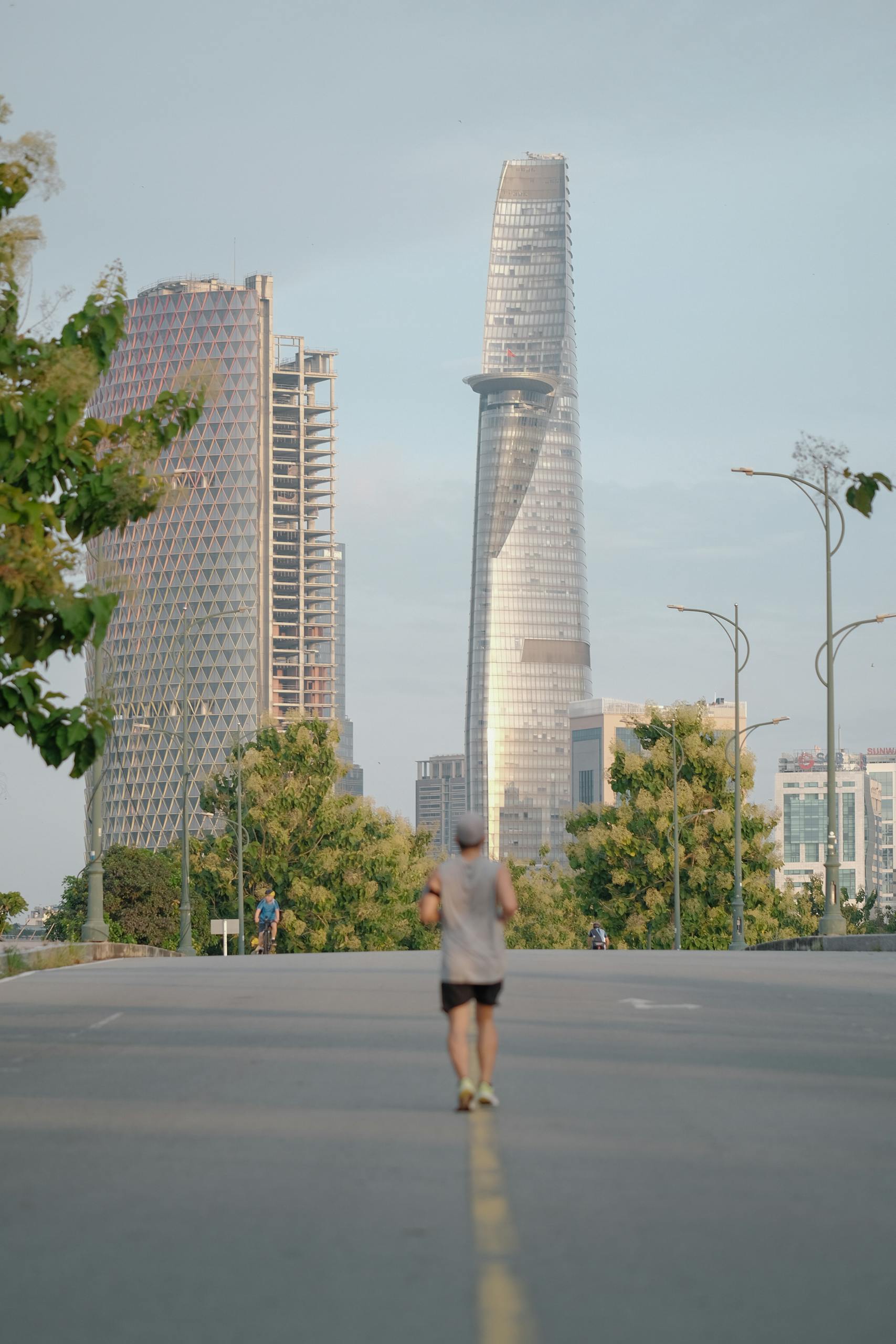 A person jogging on a city street with the Bitexco Financial Tower in the skyline of Ho Chi Minh City, Vietnam.